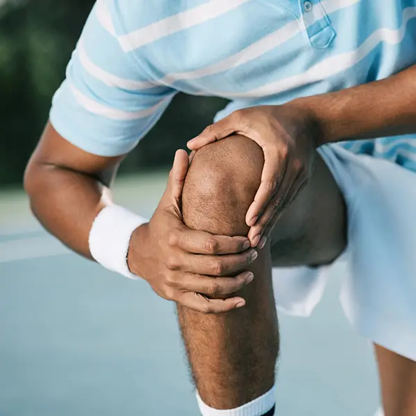 Person holding their knee in pain while playing tennis, illustrating knee discomfort treated by Genicular Artery Embolization