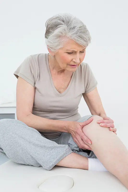 Older adult holding her knee in pain, representing chronic knee discomfort often treated with Genicular Artery Embolization (GAE)